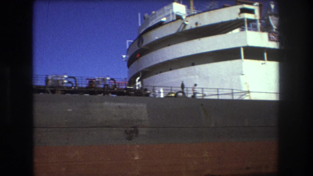 1975 Boston 8mm frame showing a large white passenger ship docked at port, with upper decks, railings, and small figures visible from a low obstructed viewpoint.