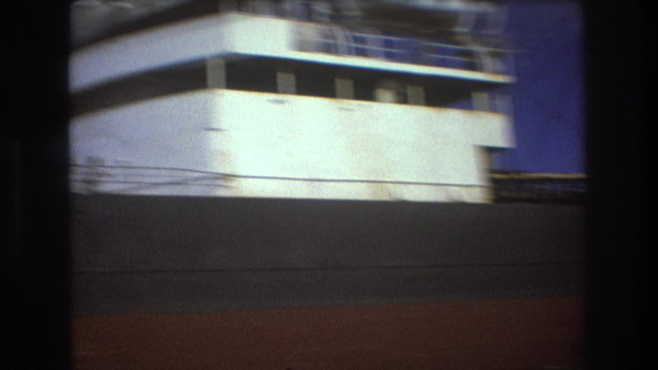 Final 1975 Boston frame showing the side and upper structure of the white passenger ship, with motion blur, dark foreground obstruction, and blue sky at the edge.