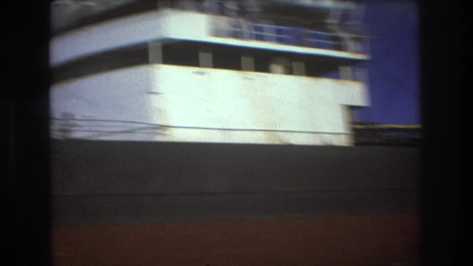 Final 1975 Boston frame showing the side and upper structure of the white passenger ship, with motion blur, dark foreground obstruction, and blue sky at the edge.