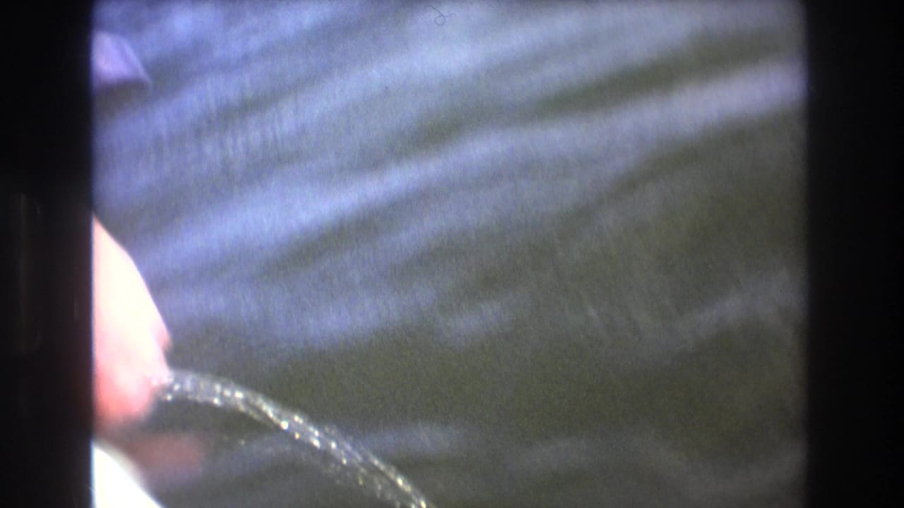 1975 Boston 8mm frame showing rippled water through dark boat-side framing, with a partial hand or arm visible at the left edge.