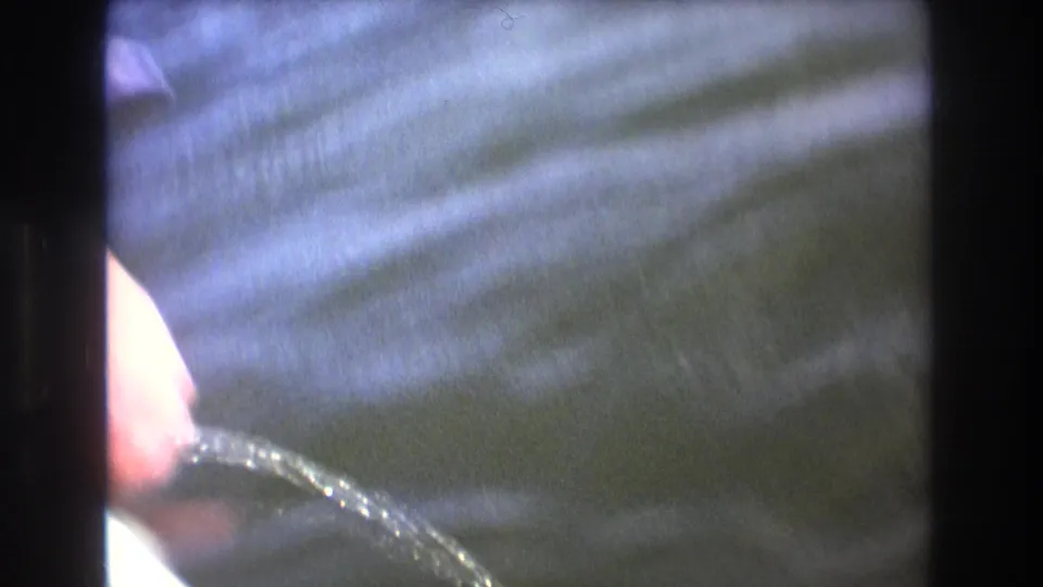 1975 Boston 8mm frame showing rippled water through dark boat-side framing, with a partial hand or arm visible at the left edge.