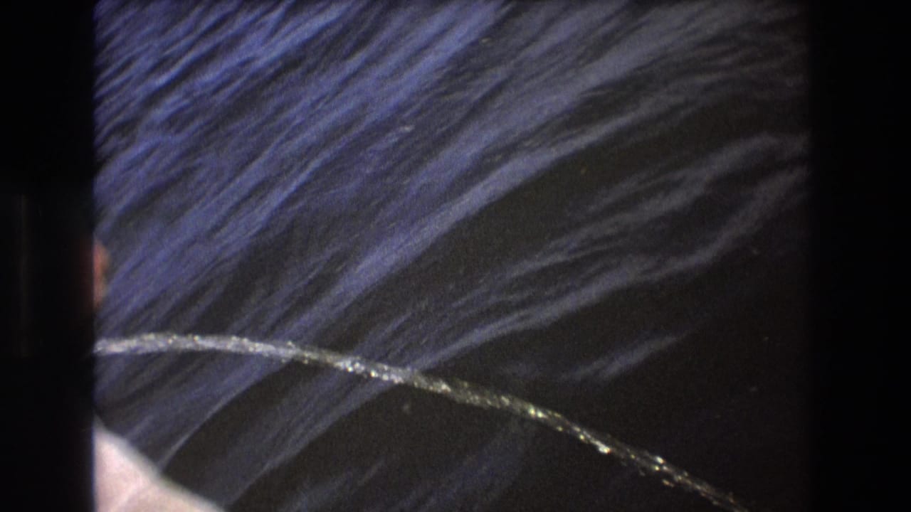 1975 Boston 8mm frame showing a bright stream entering from the left edge and arcing over dark rippled water beside the boat.