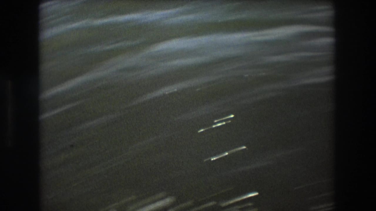 1975 Boston 8mm frame showing rippled green-blue water with bright streaks and dark boat-side borders on both sides.