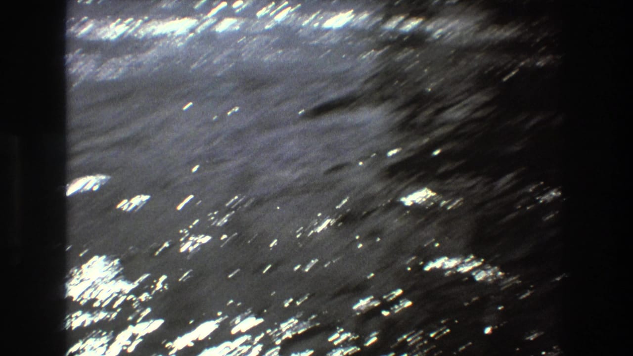 Sun glare sparkles across rippling water in archival 8mm footage associated with Boston in 1975, with no boat yet clearly centered in the frame.
