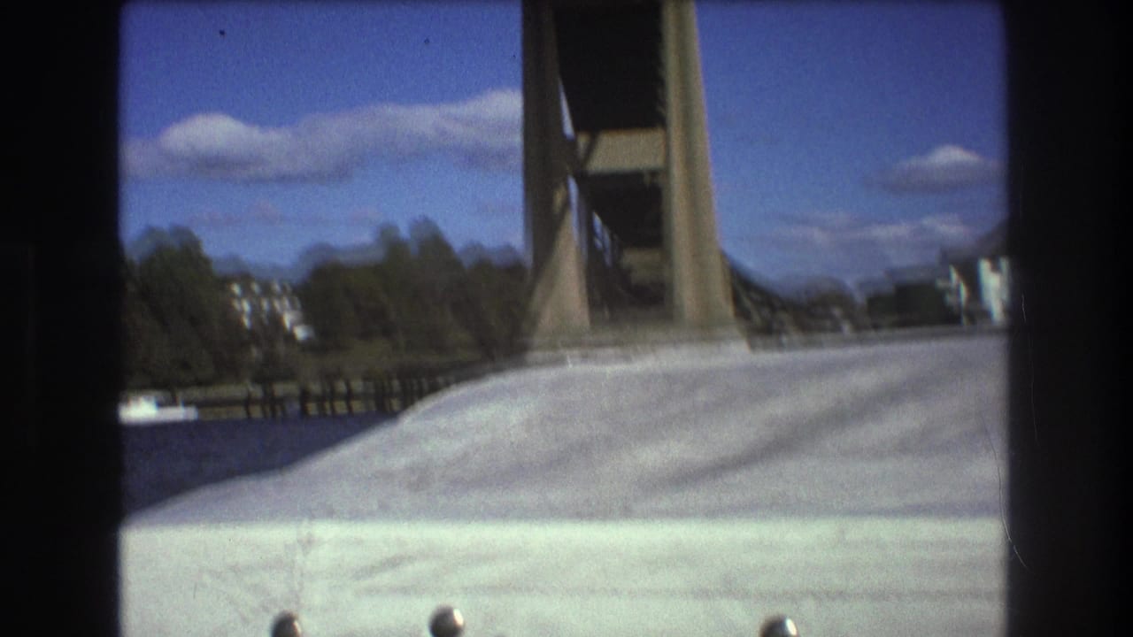 1975 Boston 8mm frame from a boat, showing a white deck or bow pointed toward a large bridge structure under blue sky and clouds.