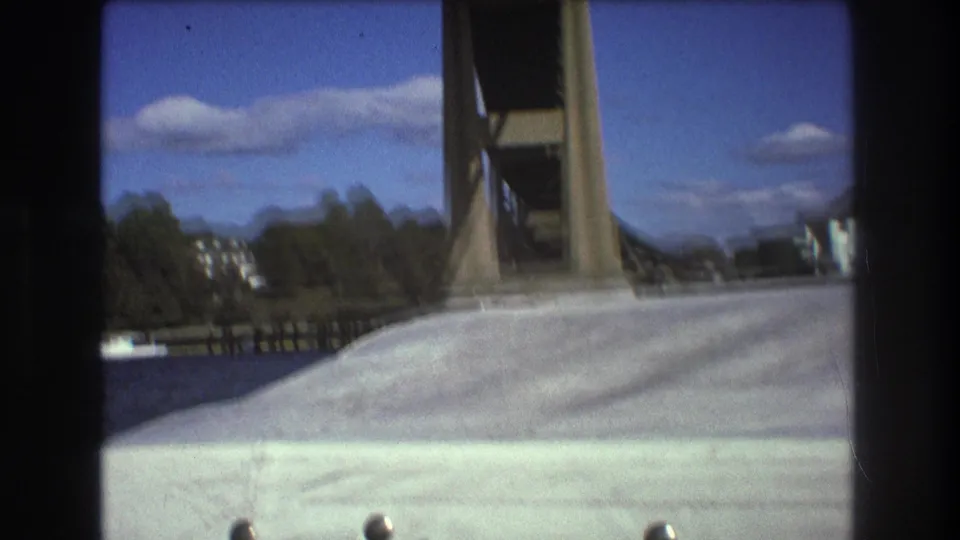 1975 Boston 8mm frame from a boat, showing a white deck or bow pointed toward a large bridge structure under blue sky and clouds.
