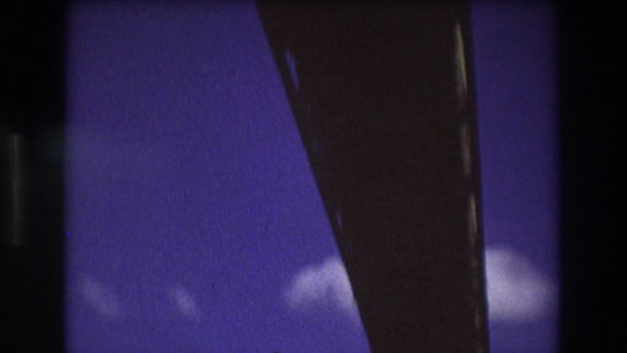 Soft 8mm frame from the 1975 Boston clip showing a dark bridge or boat structure cutting across blue sky with small clouds visible below.