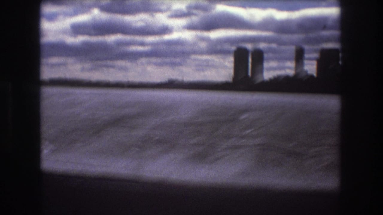 Boston, 1975, seen from a moving boat with choppy bay water in the foreground, a silhouetted skyline in the distance, and dark interior framing around the view.