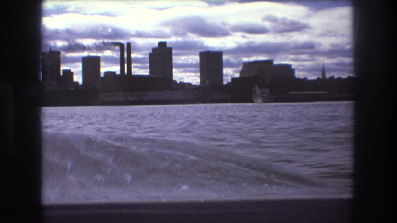 Boston, 1975, waterfront skyline viewed from a boat, showing rippled water, wake trails, dark building silhouettes, and industrial-looking vertical stacks.