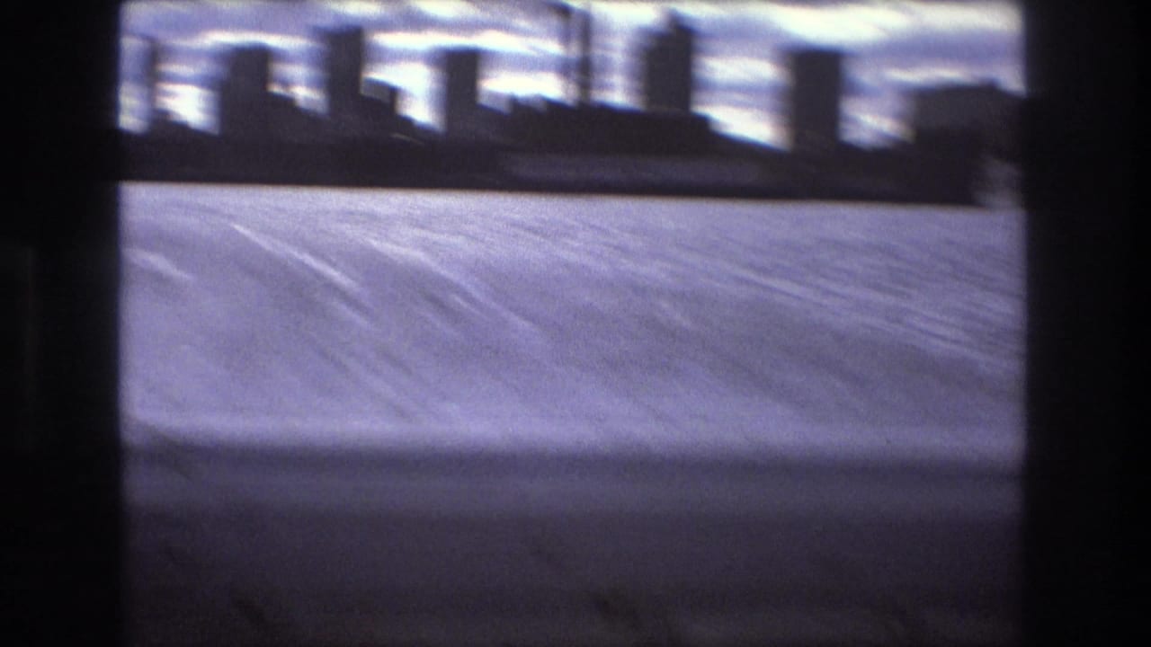 Blurred 1975 Boston waterfront view from a fast-moving boat, with choppy water, distant buildings, cloudy sky, and dark 8mm frame edges.