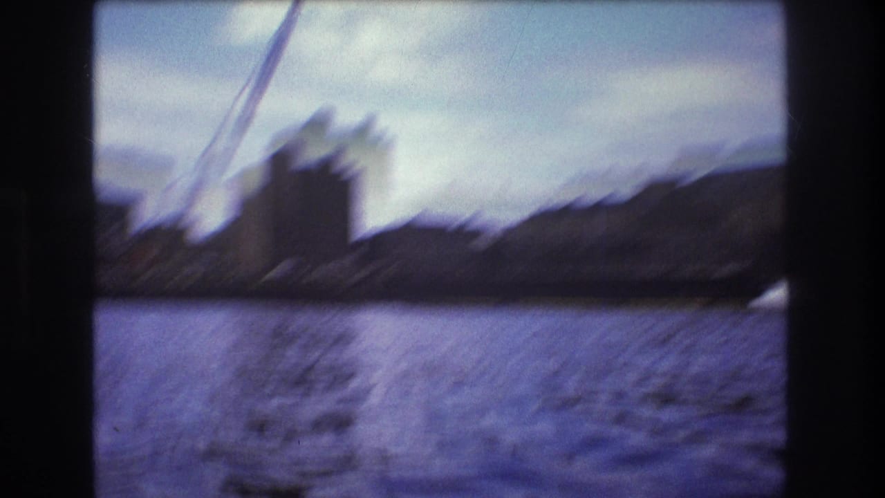 Blurred 1975 Boston waterfront construction view from a fast boat, with a crane, dark building mass, shoreline, water reflections, and visible 8mm frame edge.