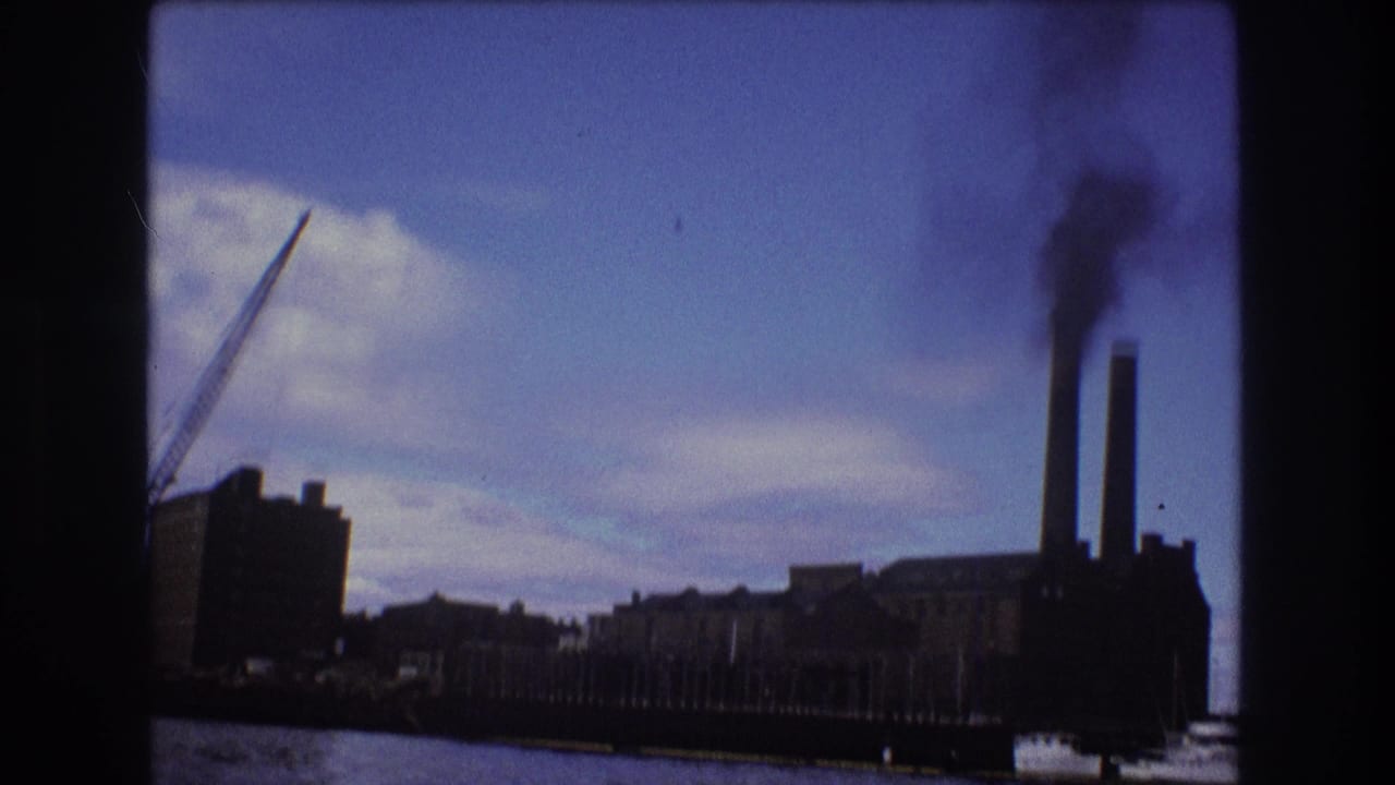 Factory buildings and two smokestacks seen from across the water with a crane nearby.