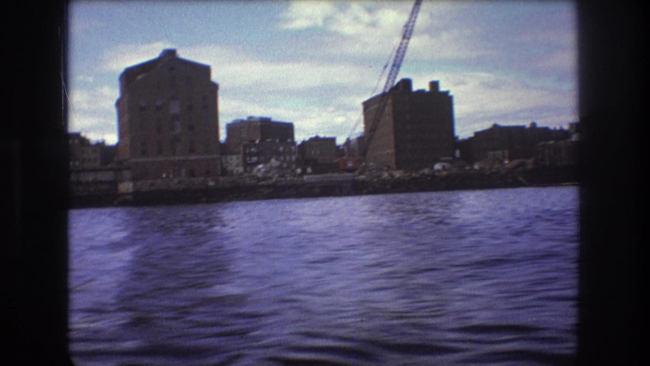 1975 Boston 8mm frame with rippling water in the foreground and industrial waterfront buildings plus a crane in the distance.