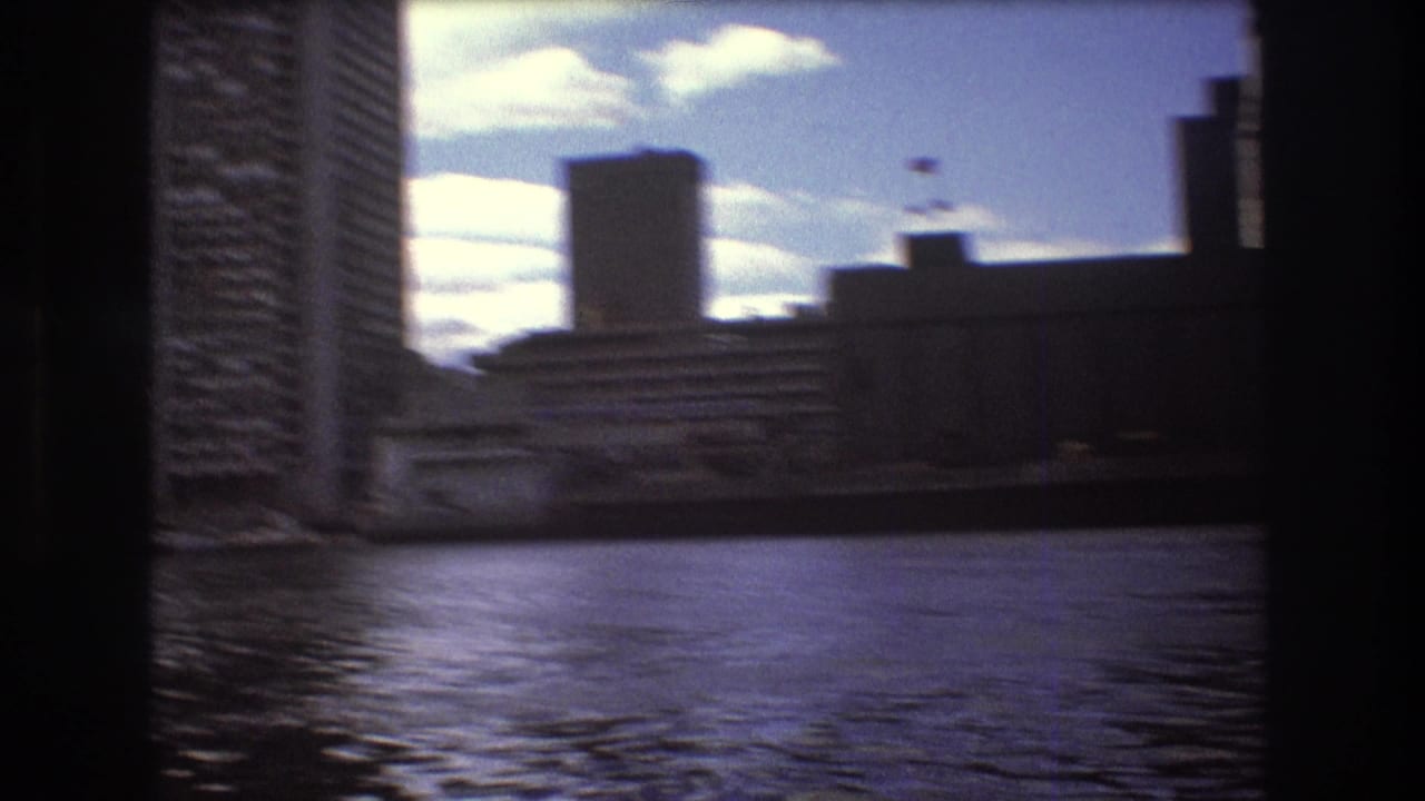 Soft 1975 Boston boat-view frame with rippled bay water, high-rise buildings, waterfront structures, and dark film borders.