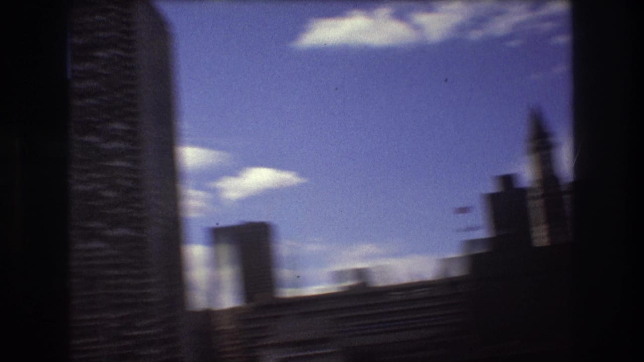 A moving-boat view of Boston skyscrapers, with a tall dark building passing close to frame and softer waterfront forms in the background.