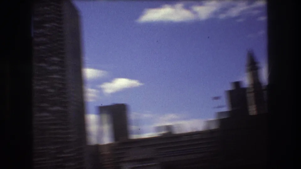 A moving-boat view of Boston skyscrapers, with a tall dark building passing close to frame and softer waterfront forms in the background.