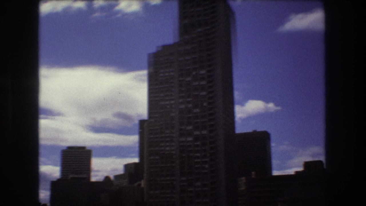 1975 8mm home-movie view of the Boston harbor skyline from a moving boat, with dark framing edges, silhouetted buildings, and bright cloud cover.