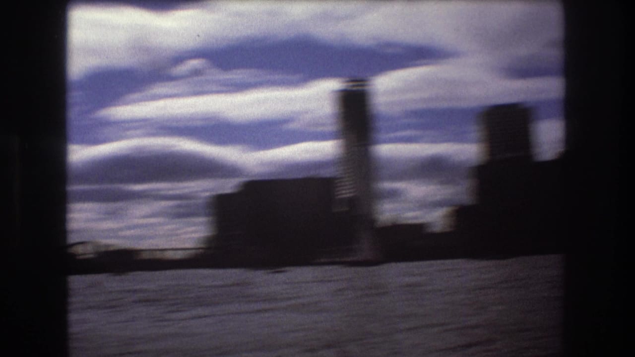 Soft 8mm frame of Boston harbor and skyline from a moving boat, with motion blur, dark framing edges, water in the foreground, and bright clouds overhead.