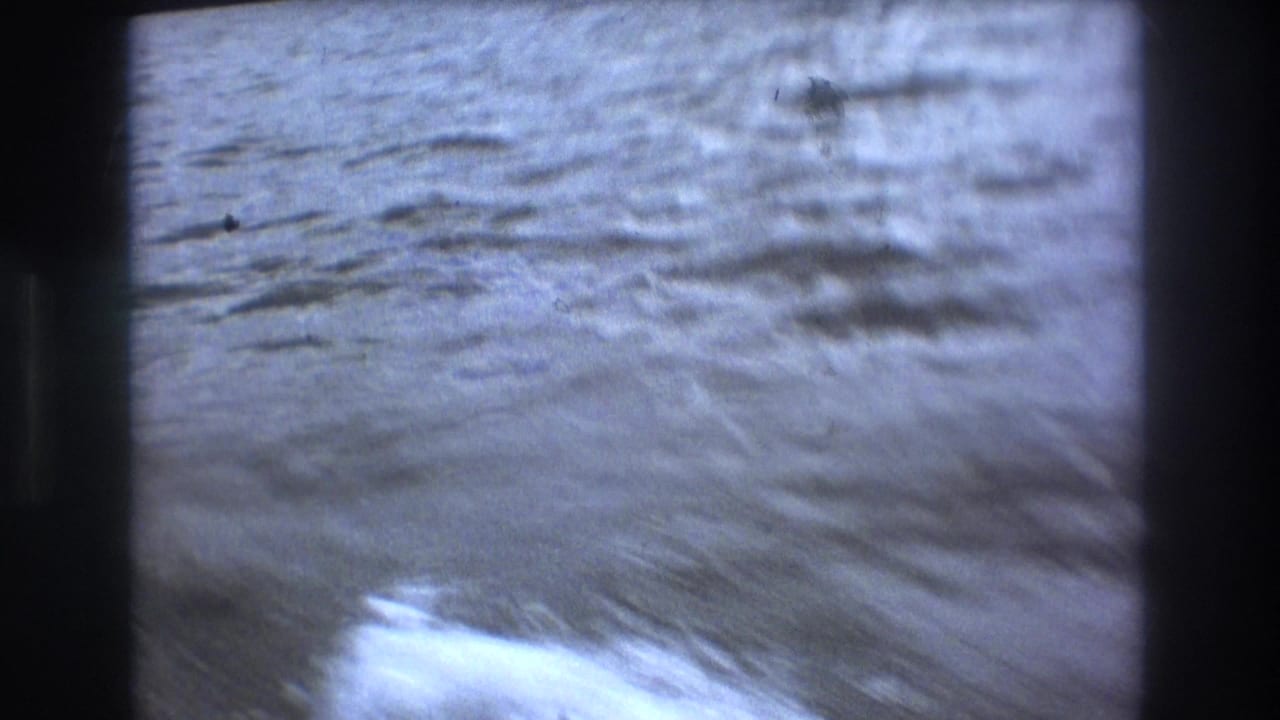 Boston 1975 8mm frame showing blurred rippled water and a pale boat wake during fast handheld movement from a watercraft.