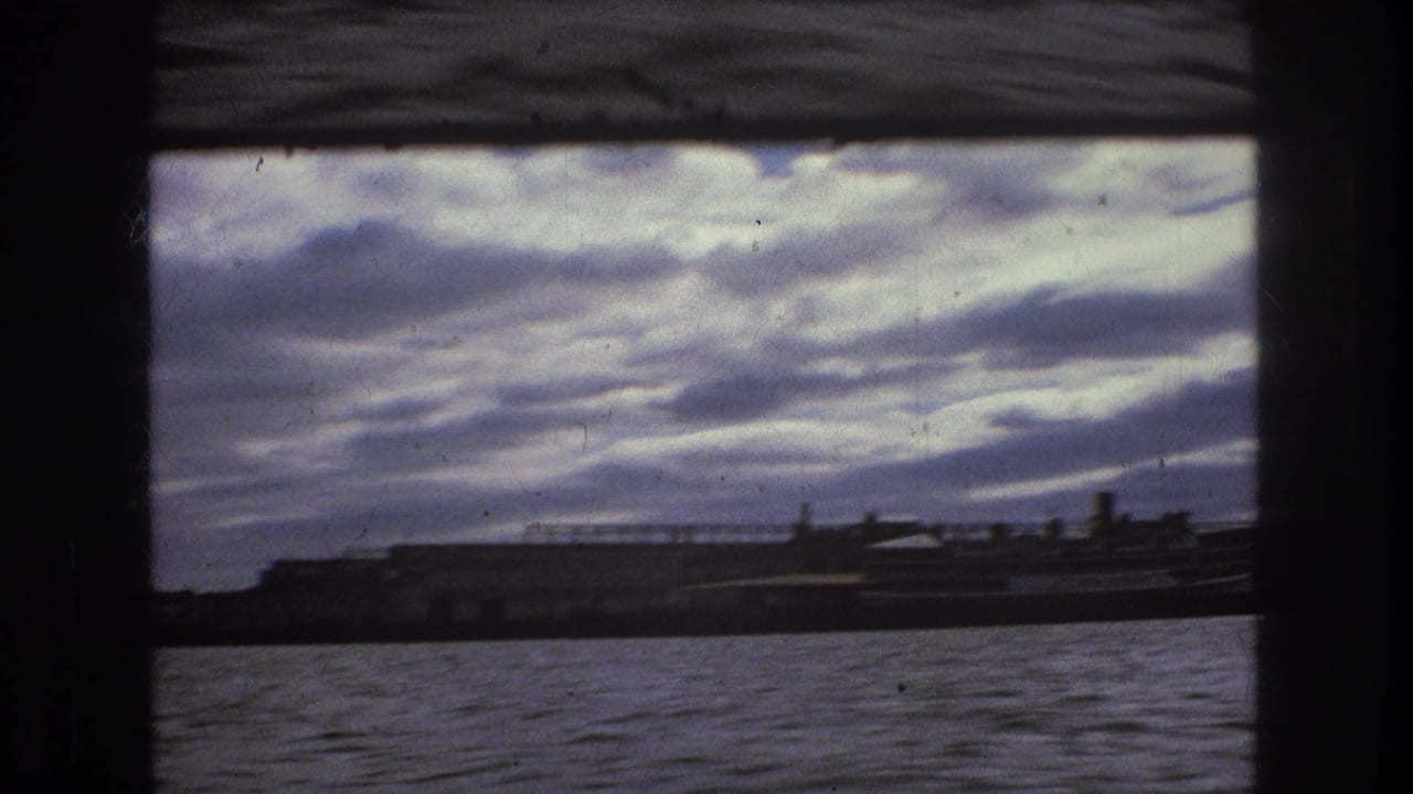 Boston-area harbor view from a moving vessel, with choppy water, low industrial forms, and a dramatic clouded sky in faded 8mm color.