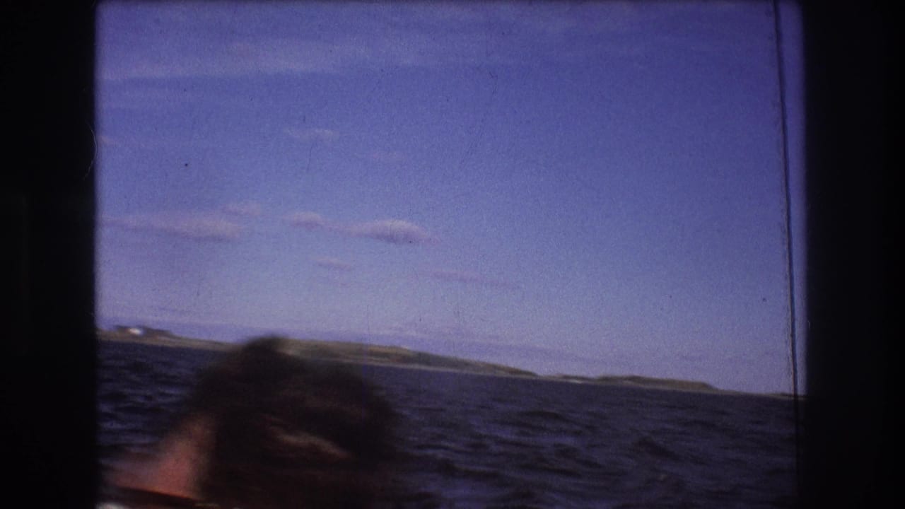 1975 Boston-area 8mm frame showing choppy blue water and a low distant shoreline viewed through dark window framing from a moving boat.