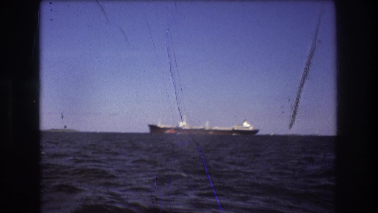 1975 Boston-area 8mm frame with a large ship traveling near the horizon, seen across choppy water through a dark boat-window opening.