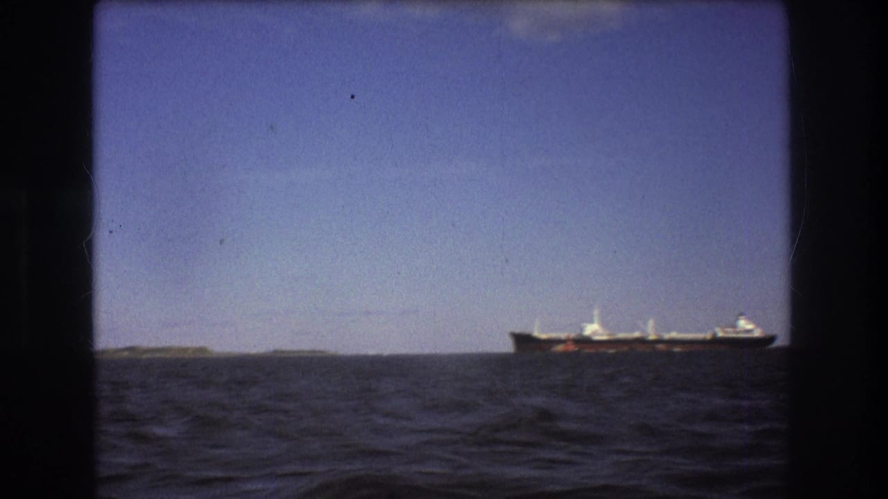 Final 8mm frame of the Boston-area ship view, showing the vessel at the right edge of the horizon beyond open water and a small stretch of land.