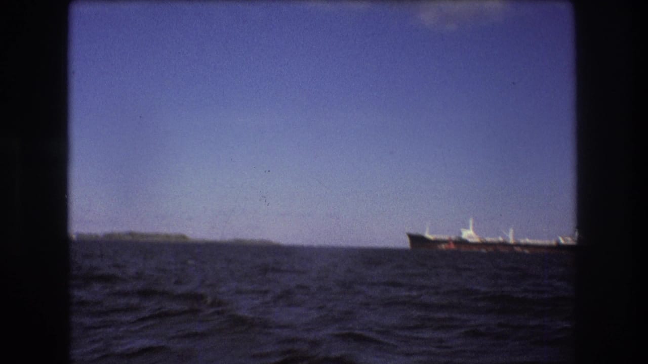 1975 Boston-area 8mm frame showing a distant large ship crossing the horizon beyond choppy open water and a low shoreline.