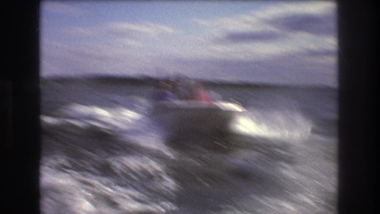 1975 Boston-area 8mm frame showing a small speedboat with passengers riding through choppy open water, with wake and spray behind it.
