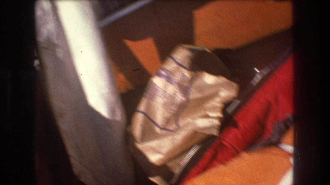 Close 8mm home-movie view of the small boat interior, with a light-colored bag, red fabric, white hull edge, and warm-toned wood visible during rough movement.
