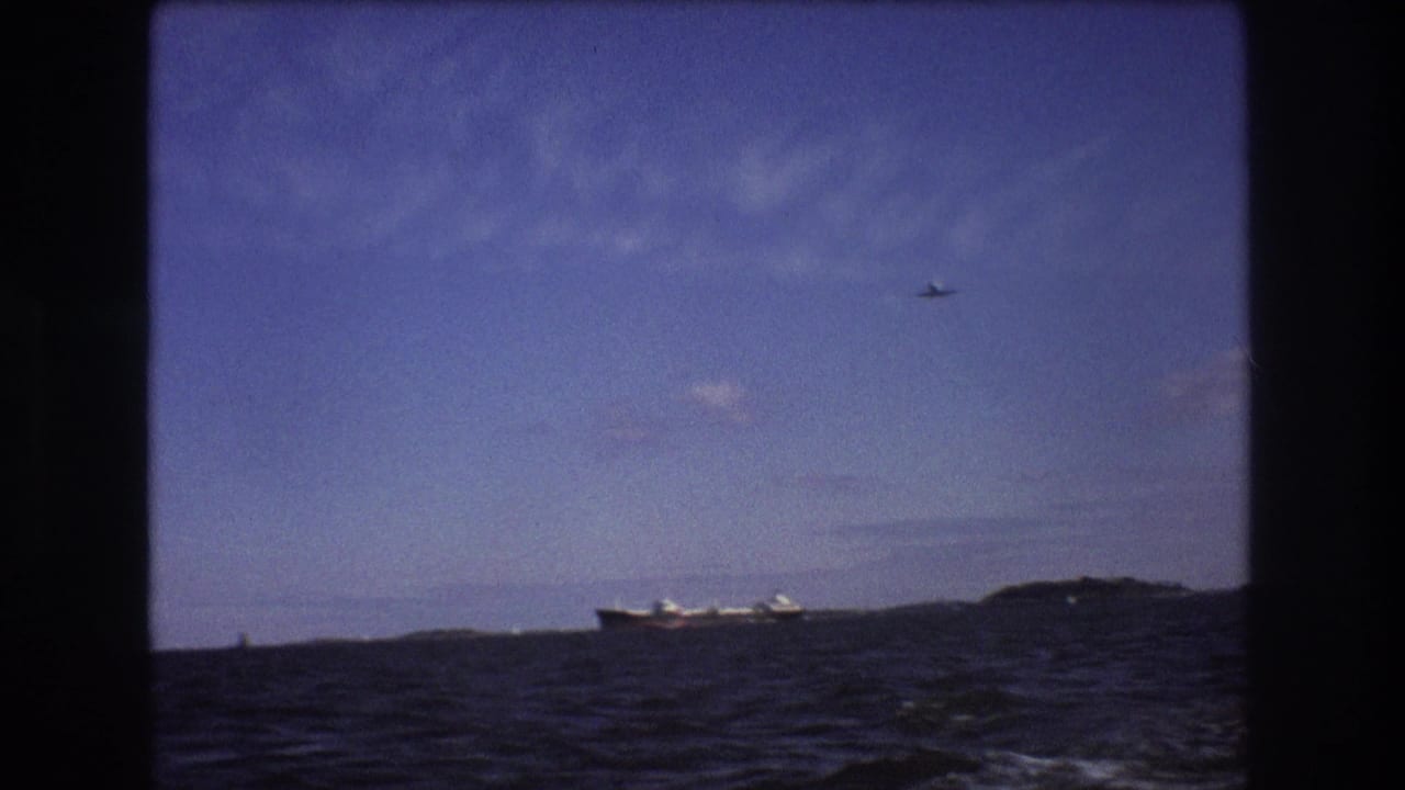 A final 1975 Boston-area boat-view frame shows choppy water, a distant ship beside low landforms, and a small aircraft high in the blue sky.