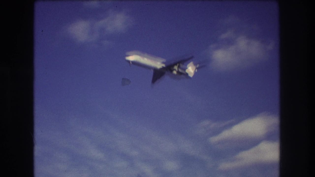 The airliner is closer in frame, seen from below against blue sky and light clouds, with the dark edges of the 8mm scan visible.