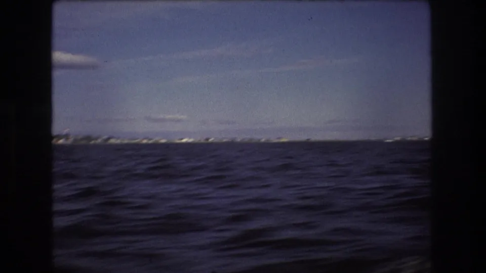 A boat-level view looks across rippled water toward a distant low shoreline, consistent with the supplied Boston waterfront setting.