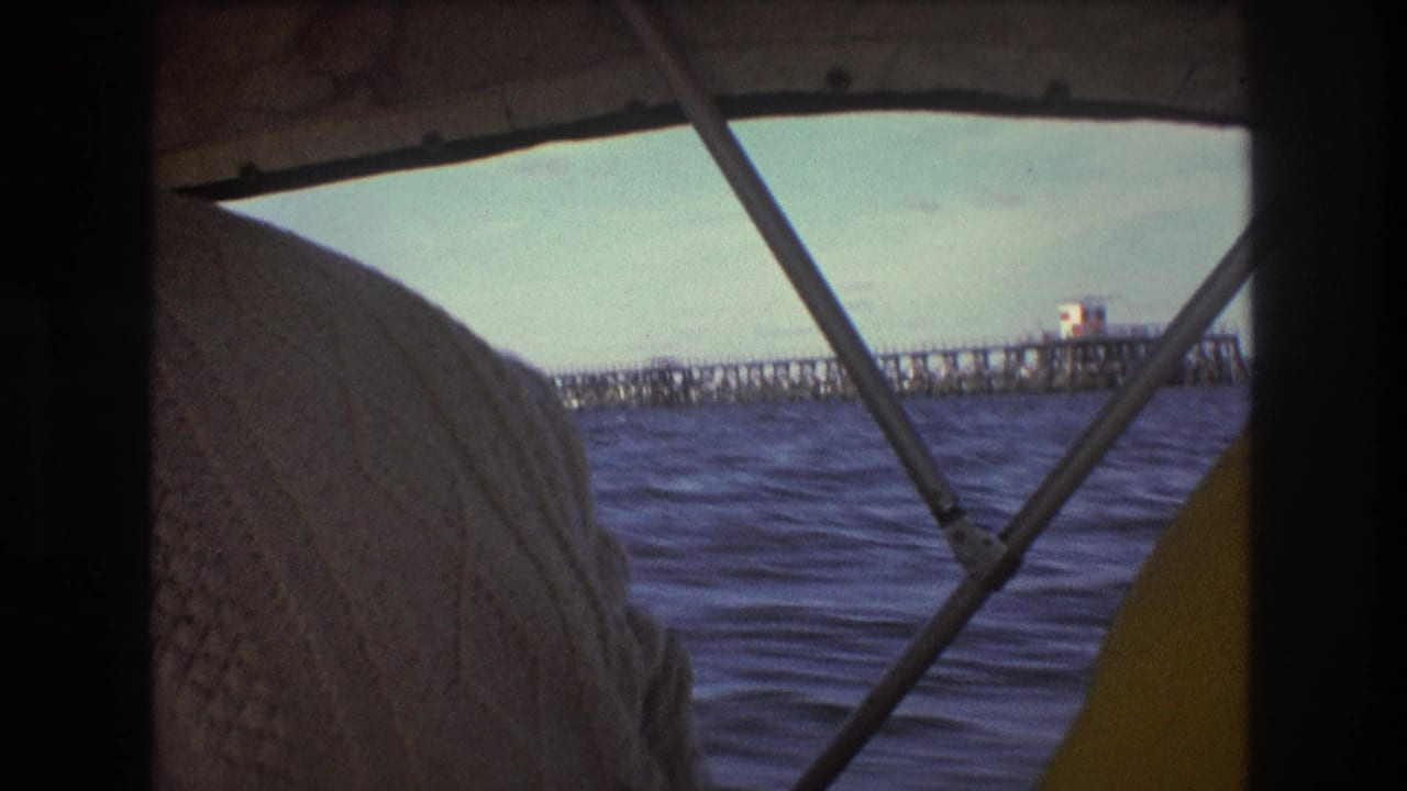 Boat passenger foreground with choppy water and a distant pier-like structure beyond the canopy.