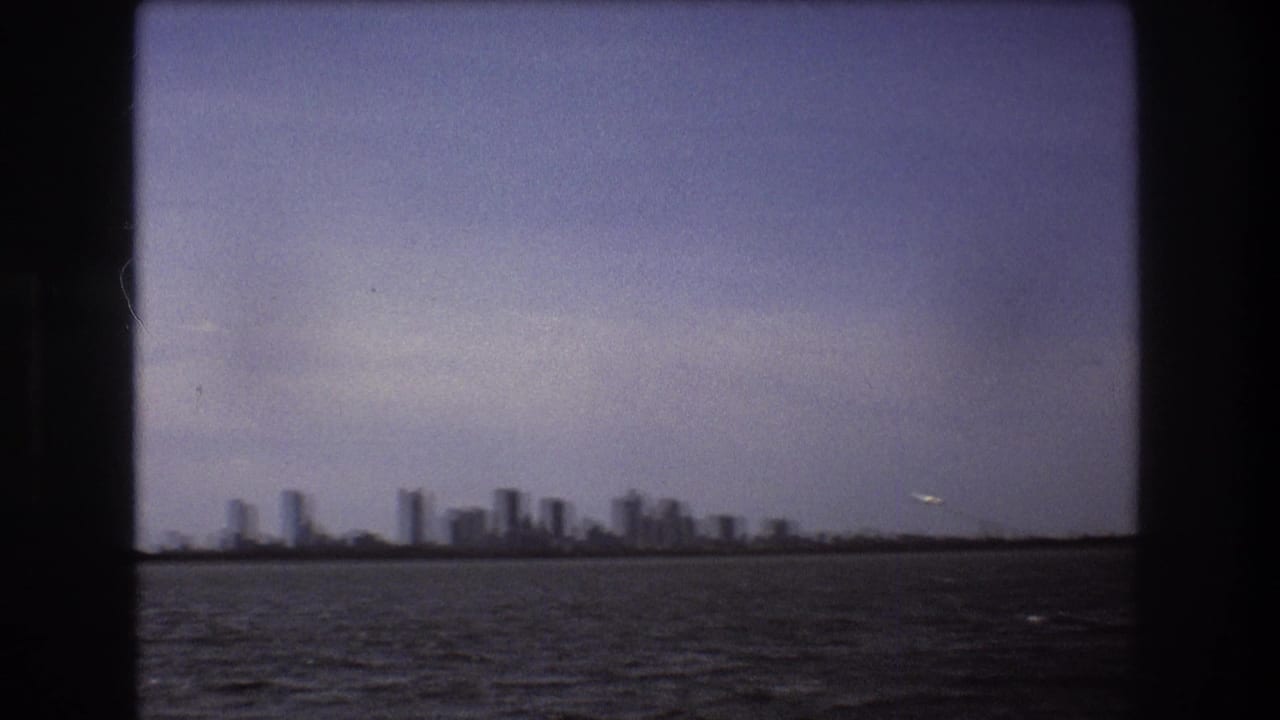 A later 1975 Boston home-movie frame shows the skyline softened by distance and film focus, with rippled water below and a small airplane near the right horizon.