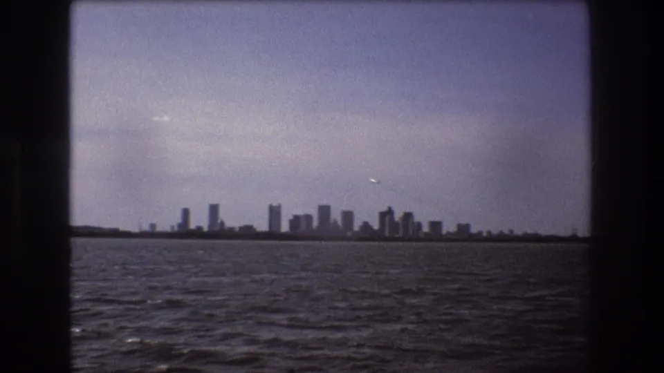 Boston skyline seen from a moving boat on the harbor, with choppy water in the foreground and softened 8mm exposure.