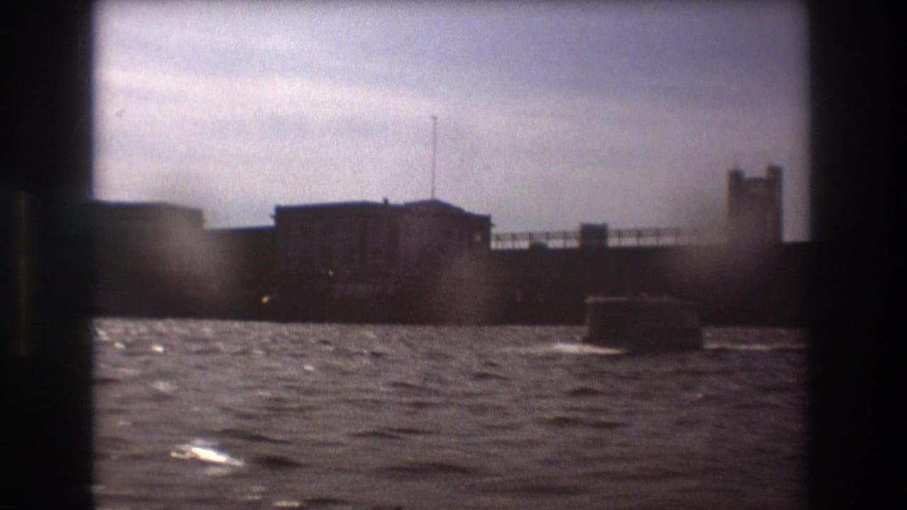 Closer Boston harbor view showing waterfront buildings, a small motorboat, and a bridge or pier structure in soft 1970s 8mm footage.