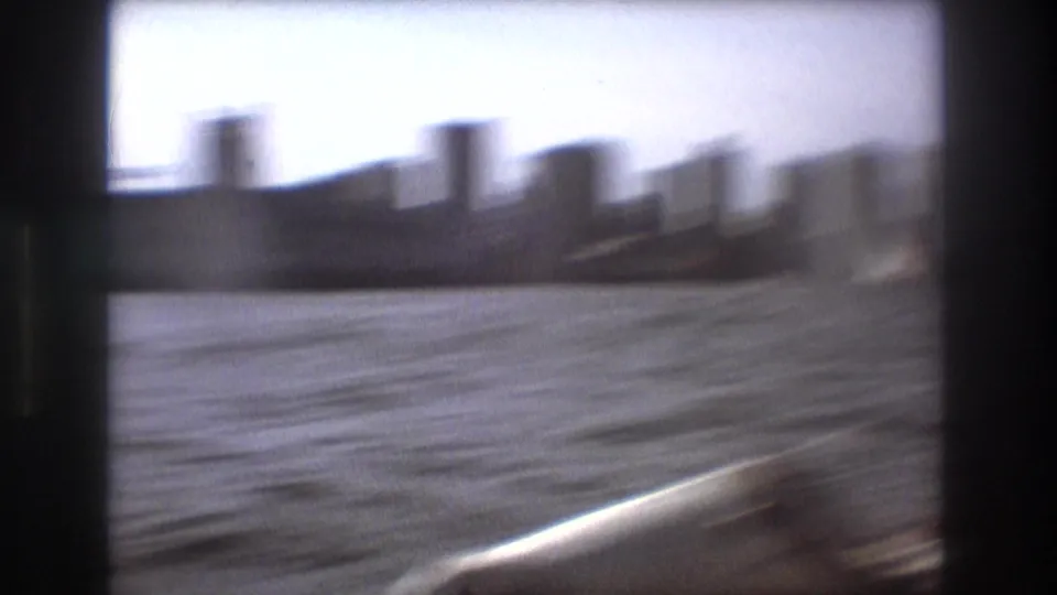 Soft, motion-blurred 1975 Boston harbor frame with distant high-rise forms, open water, and the edge of the filming boat in the foreground.