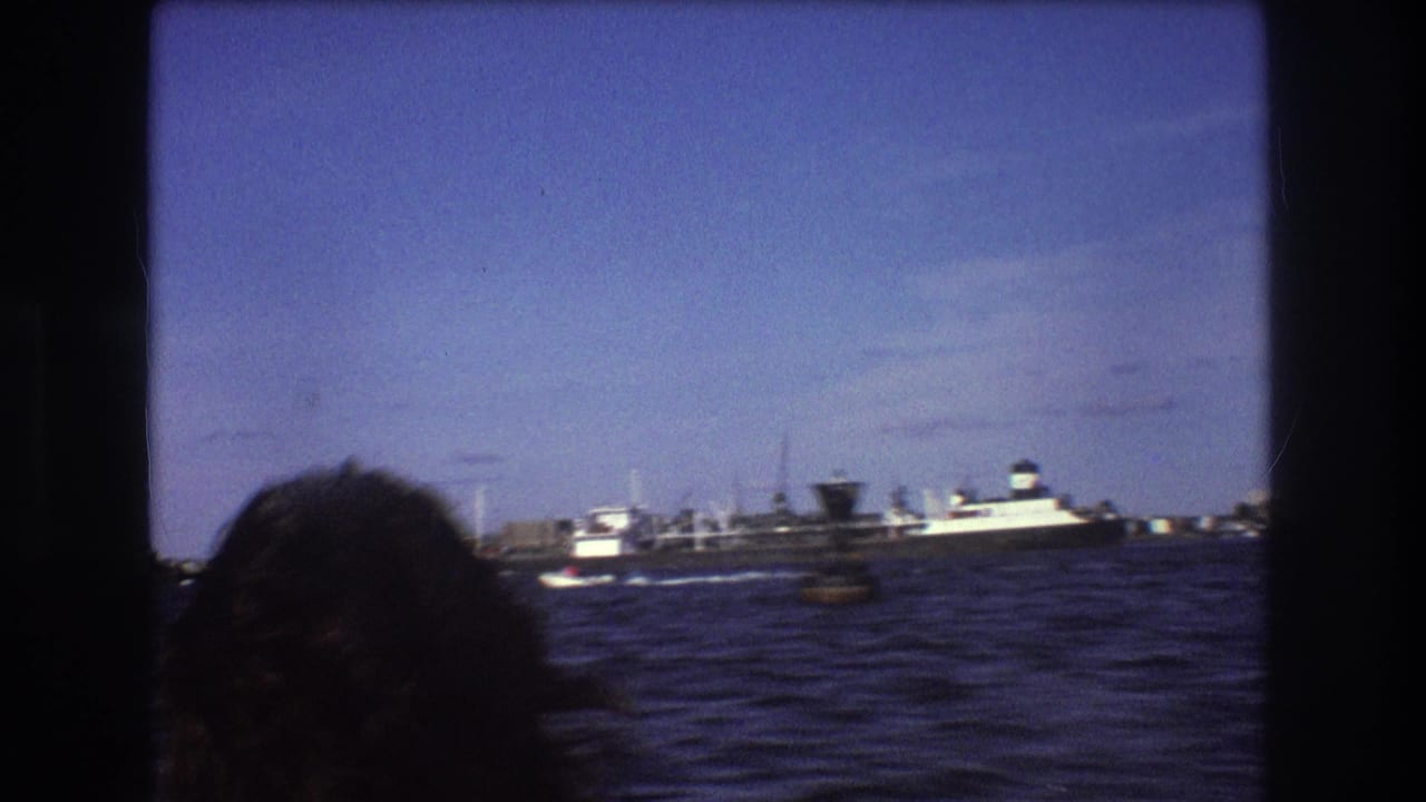 1975 Boston 8mm boating frame showing a passenger's head at lower left, rough bay water, and a large ship near distant harbor structures.