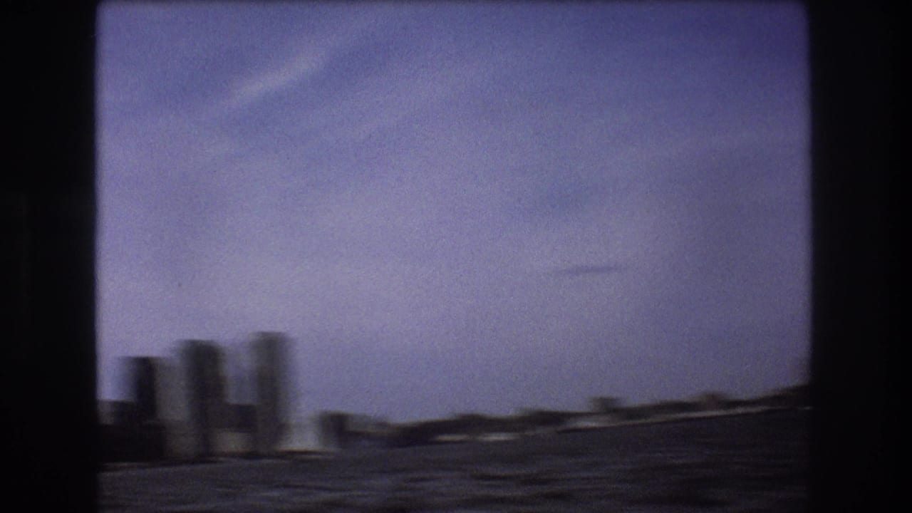 A motion-softened 1975 Boston waterfront view shows choppy harbor water, low shoreline buildings, and distant vertical structures from a moving small boat.