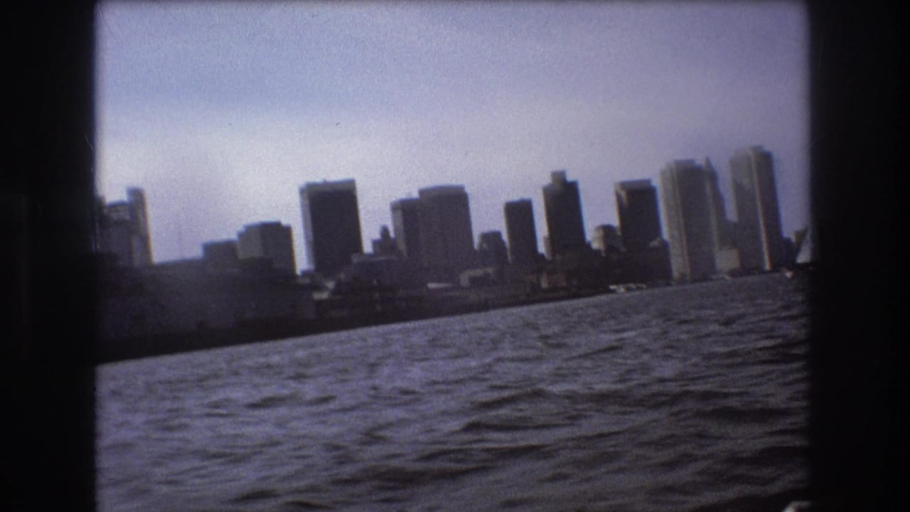 The Boston skyline appears across choppy harbor water in a slightly tilted 1975 8mm home-movie frame shot from a moving boat.