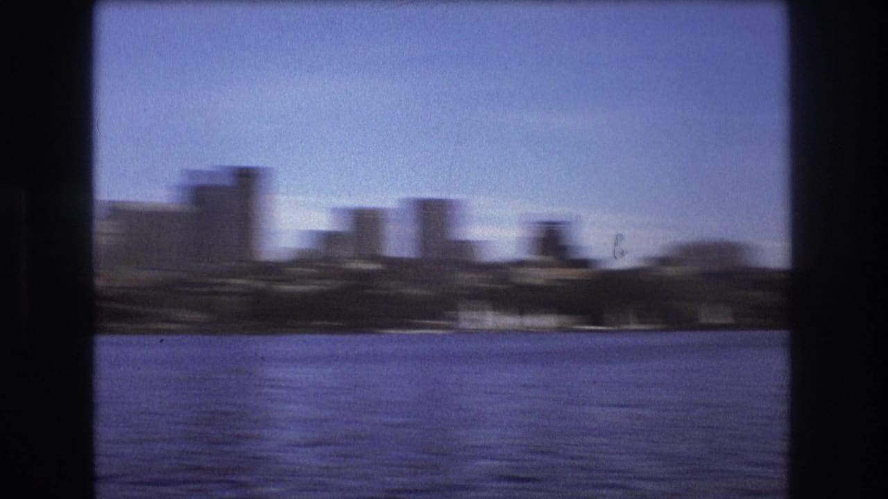 Motion-blurred 8mm view of Boston waterfront buildings and skyline across a broad stretch of blue water.
