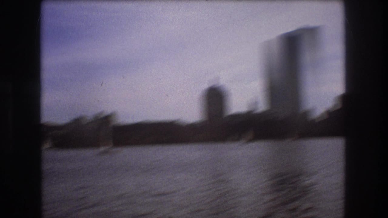 Soft-focus 8mm boat-view frame of Boston waterfront silhouettes and taller buildings across the water.