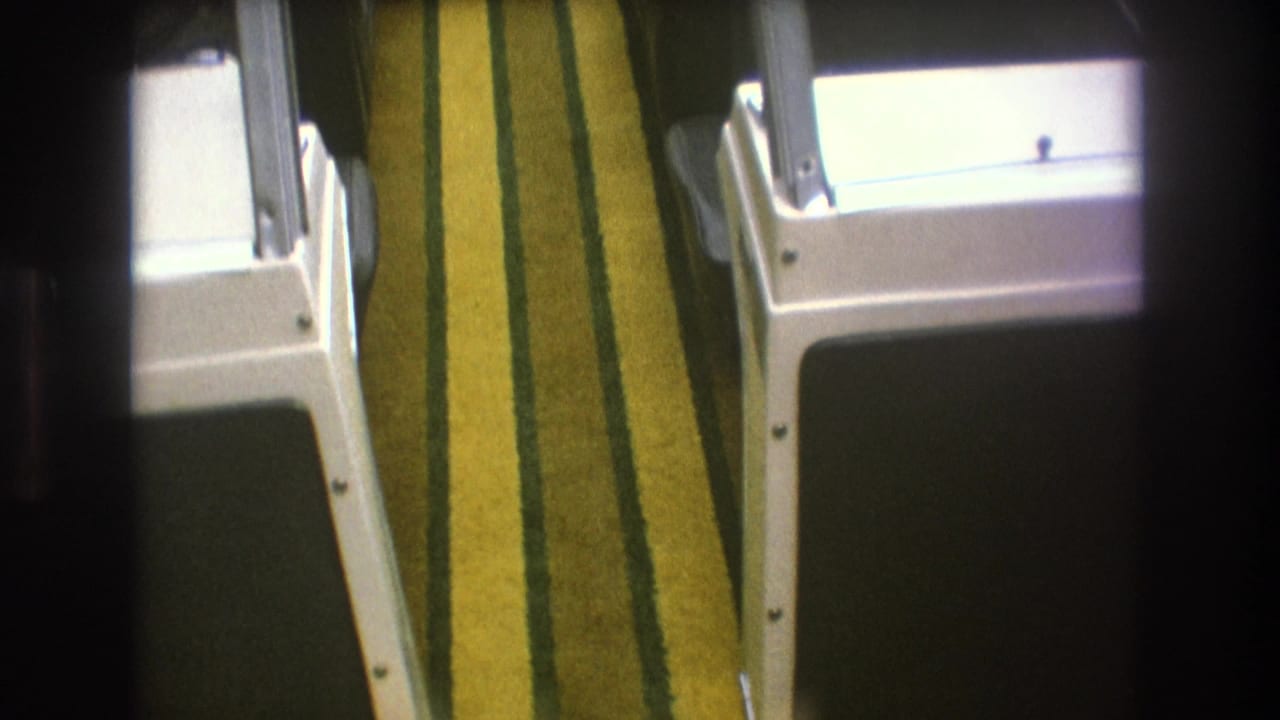 Handheld 8mm view of a boat interior with yellow and green striped carpet, white molded cabin fixtures, and dark vinyl seating or panels.