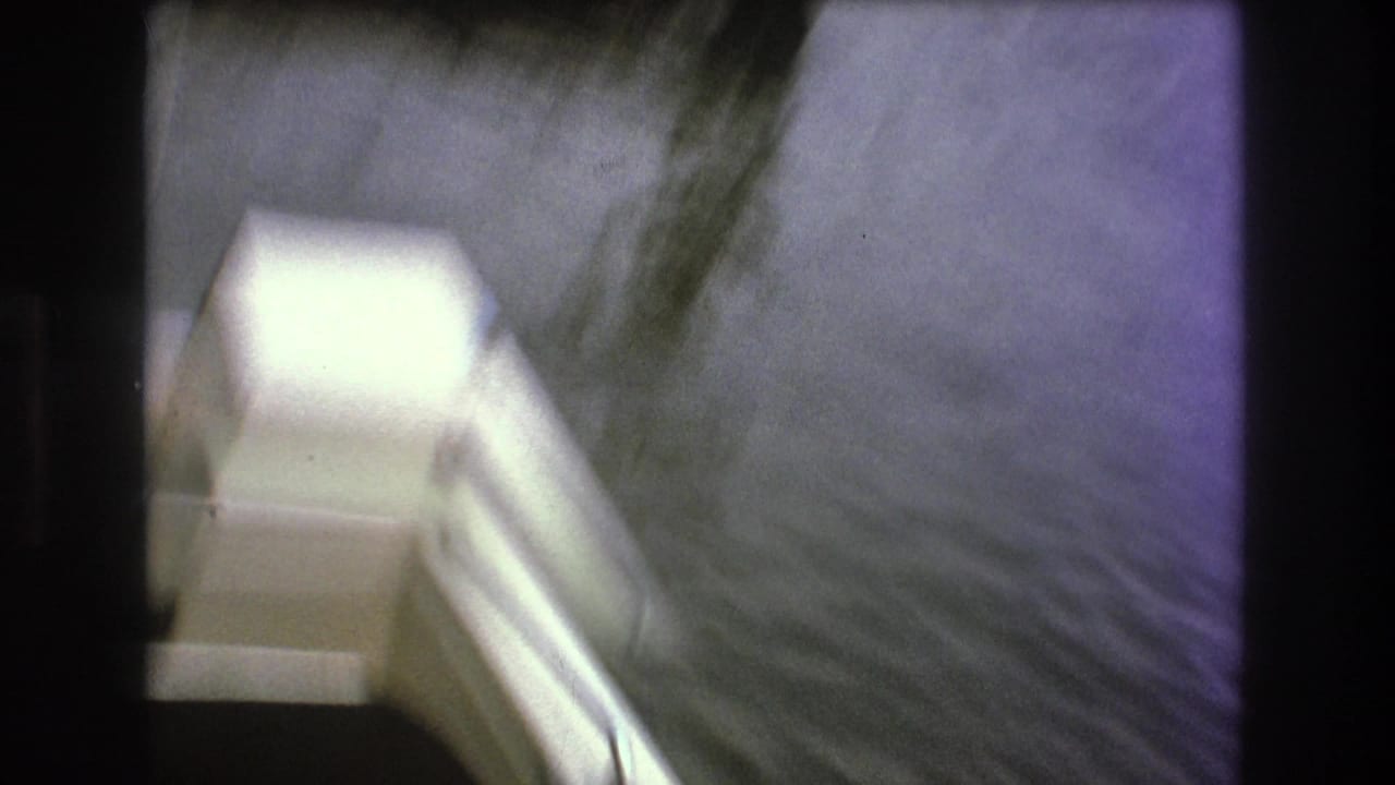 Faded 8mm frame from the 1975 Boston-labeled clip showing a red water ski or boat equipment near a striped deck with lake water alongside.