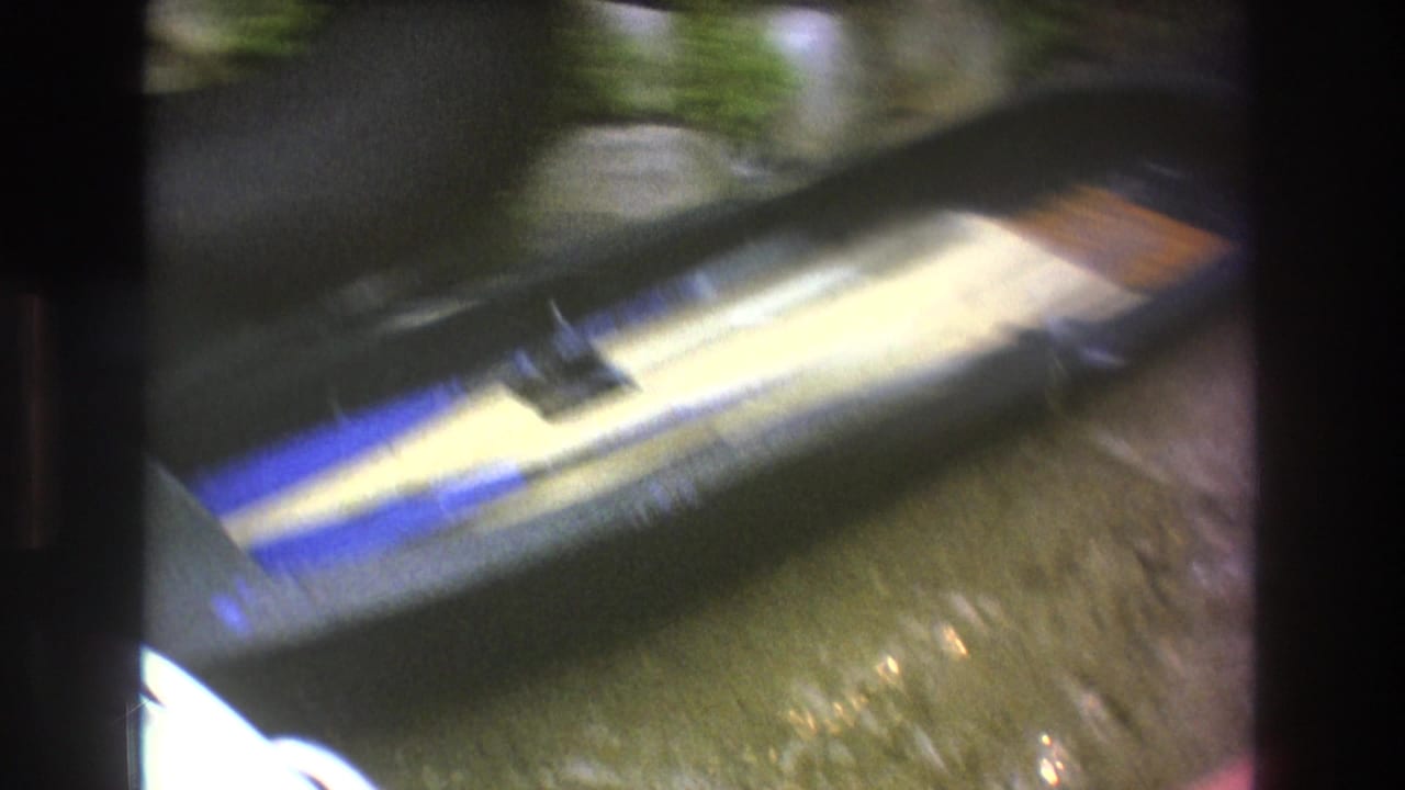 A motion-blurred 8mm frame shows a striped water ski or boat gear near wet ground and greenery as the camera moves close to the equipment.