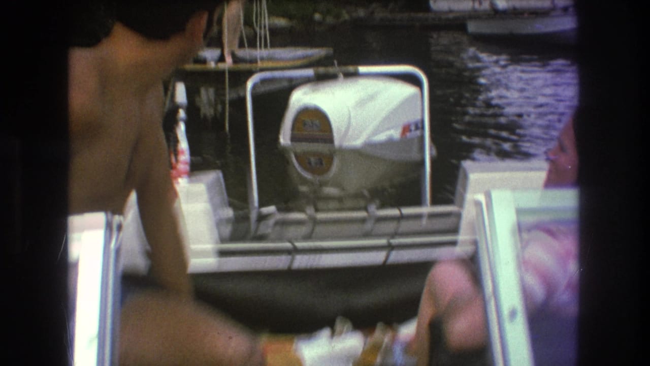 Candid 1975 Boston 8mm frame with partial figures on a small motorboat, water behind them, and the white outboard motor centered in view.