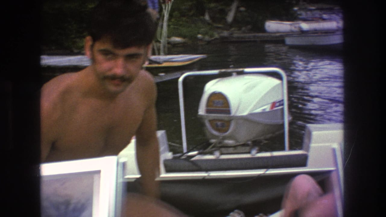 1975 Boston 8mm frame showing a shirtless man with a mustache and a seated woman on a small motorboat, with the white outboard engine prominent behind them.