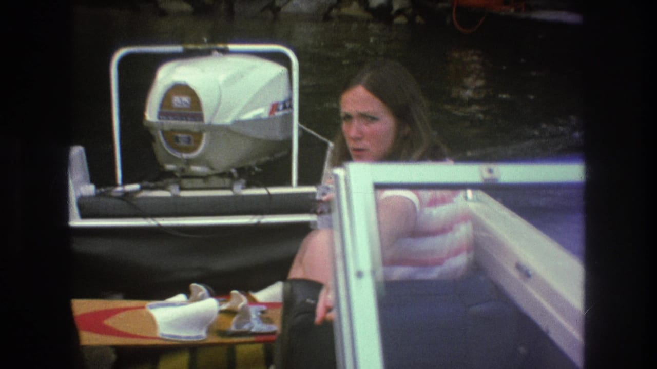 A woman in a striped shirt sits in a small motorboat beside a windshield, with a white outboard motor behind her in 1975 Super 8 footage from the supplied Boston metadata.