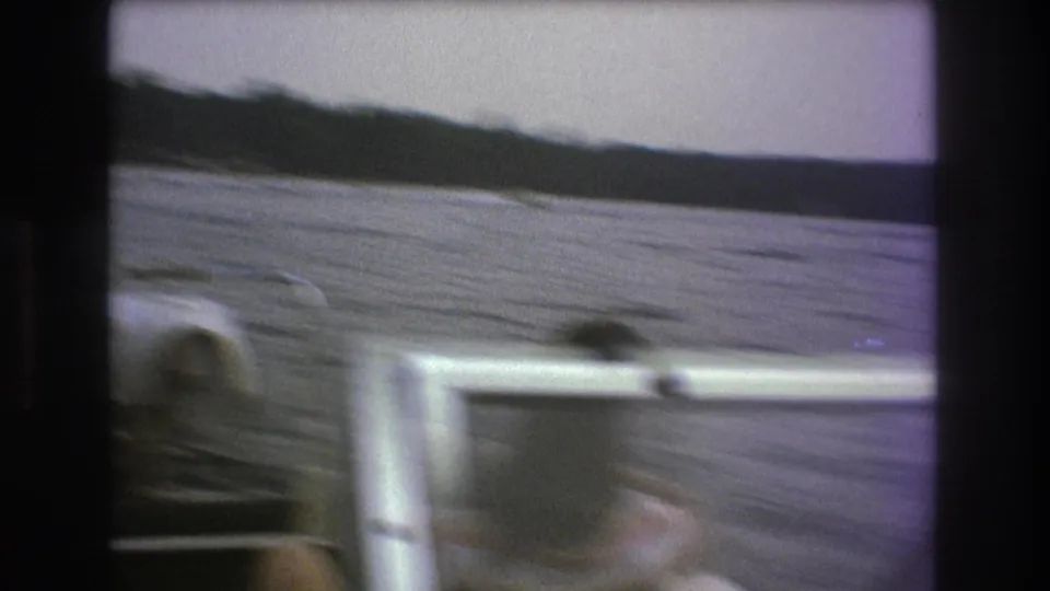 The final frame is motion-blurred as the camera shifts across the boat interior and lake, with wooded shoreline and open water still visible in the 8mm frame.